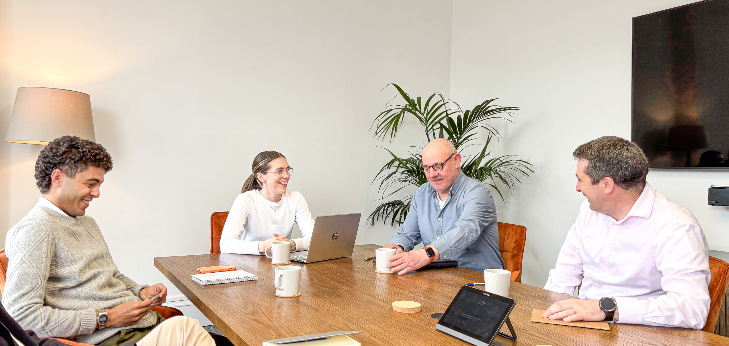 Four 56 Degrees North employees sit around the boardroom table smiling.