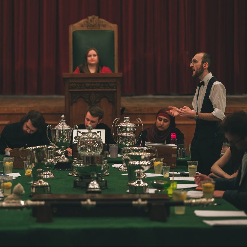 Joseph Hutchison stands at a table while debating his point.