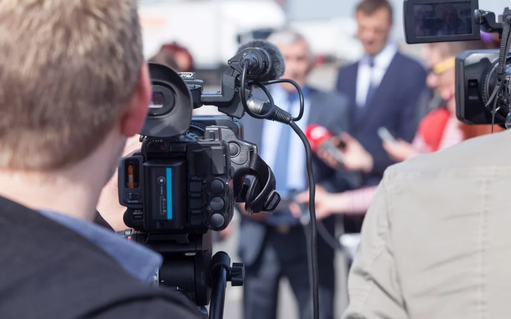 Close up of a camera man's shoulder as he interviews someone in a suit in front of him as part of a strategic communications brief.