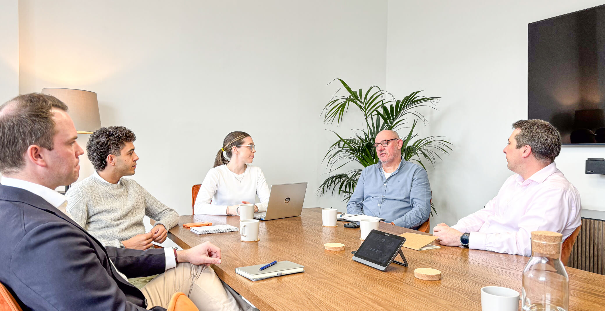 Five 56 Degrees North employees sit around the boardroom table smiling.