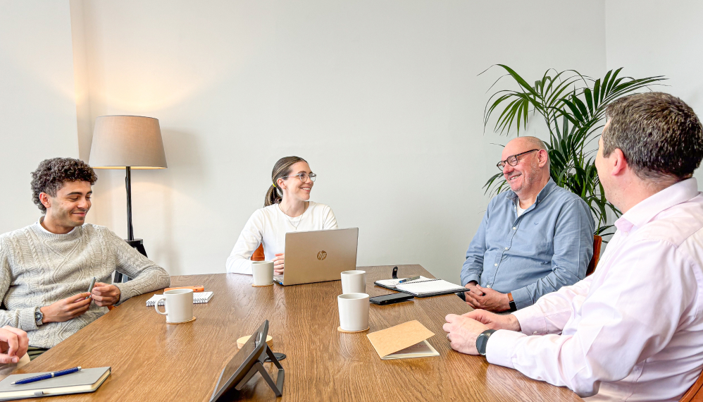 Four 56 Degrees North employees sit around the boardroom table smiling.