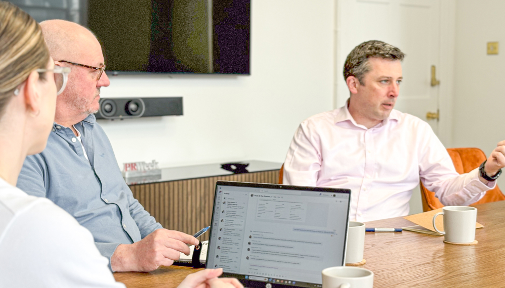 Three 56 Degrees North employees discuss something at the boardroom table.