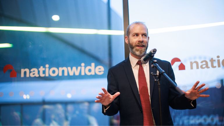 British Politician Jonathan Reynolds standing up speaking into a microphone in front of nationwide banners.