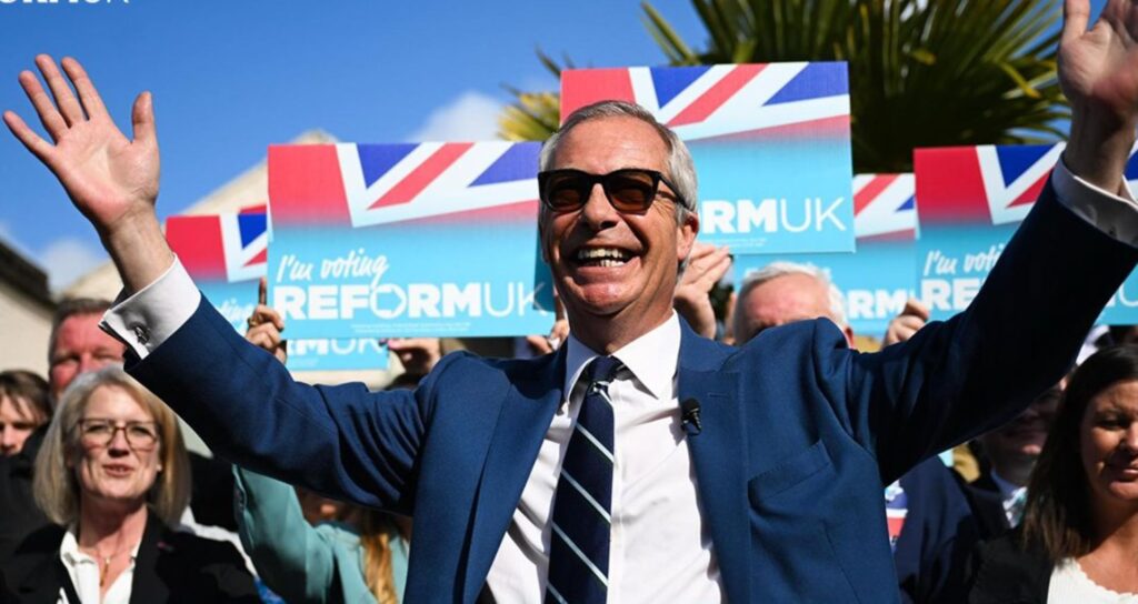 Nigel Farage of the Reform Party standing in front of British flags celebrating
