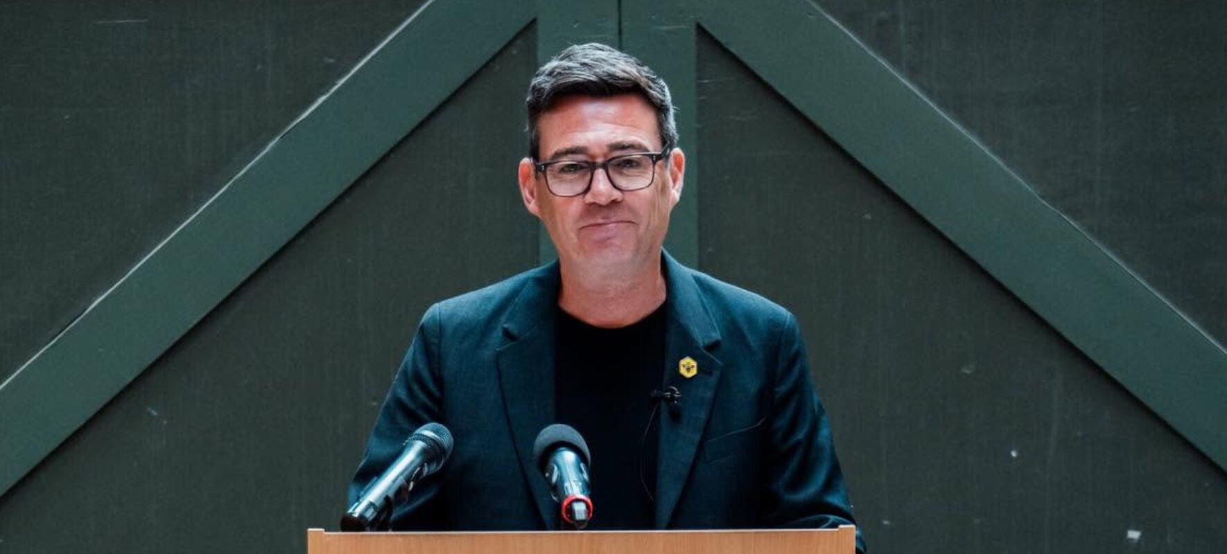 Andy Burnham standing in front of lectern